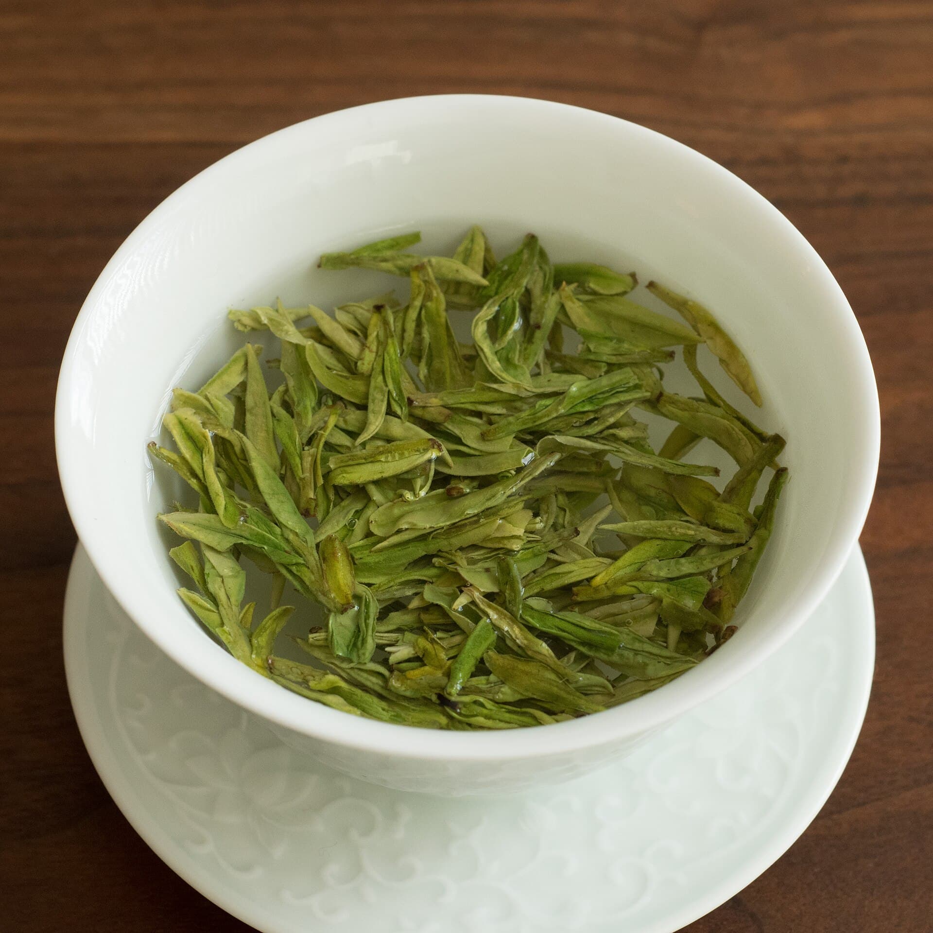Loose green tea unfurling as it steeps in a white gaiwan