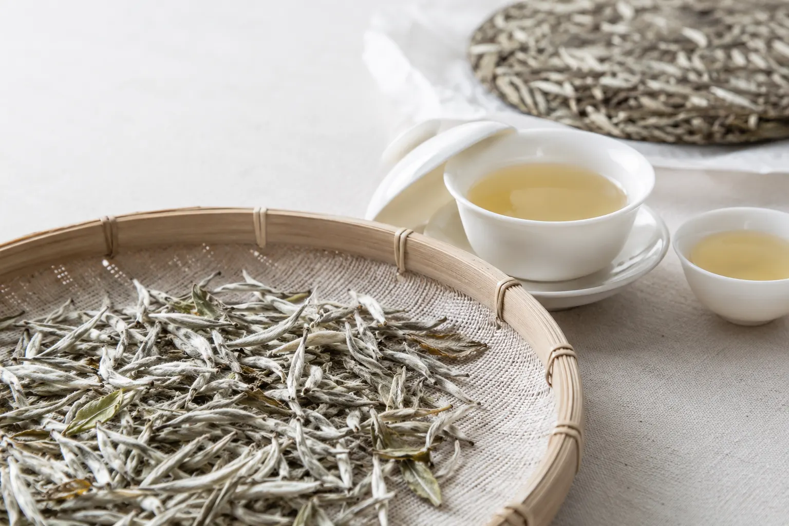 White tea buds and leaves arranged beside a pale cup of tea.